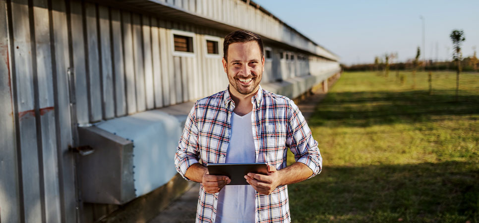 Produtor rural utilizando tablet para gestão integrada da fazenda ao lado de galpão agrícola